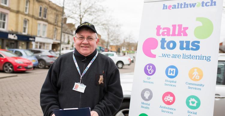 Man standing infront of a Healthwatch Talk to Us sign at a community event